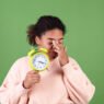 Beautiful african american woman on green background with alarm clock sleepy tired exhausted yawning