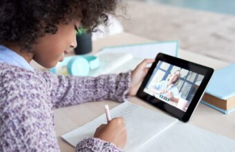 African kid child girl holding digital tablet talking with remote teacher tutor on social distance video conference call elearning online virtual class. Children learning at home, over shoulder view.
