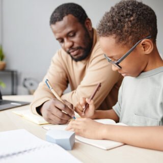 Side view portrait of African-American boy studying at home with father helping, homeschooling concept