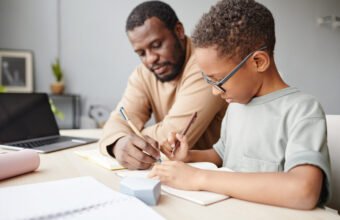 Side view portrait of African-American boy studying at home with father helping, homeschooling concept