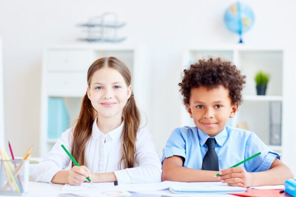 Two adorable learners sitting by desk in classroom
